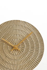 Nahaufnahme einer runden, hell goldenen Uhr mit strukturiertem Zifferblatt und goldenen Zeigern, von vorne betrachtet.