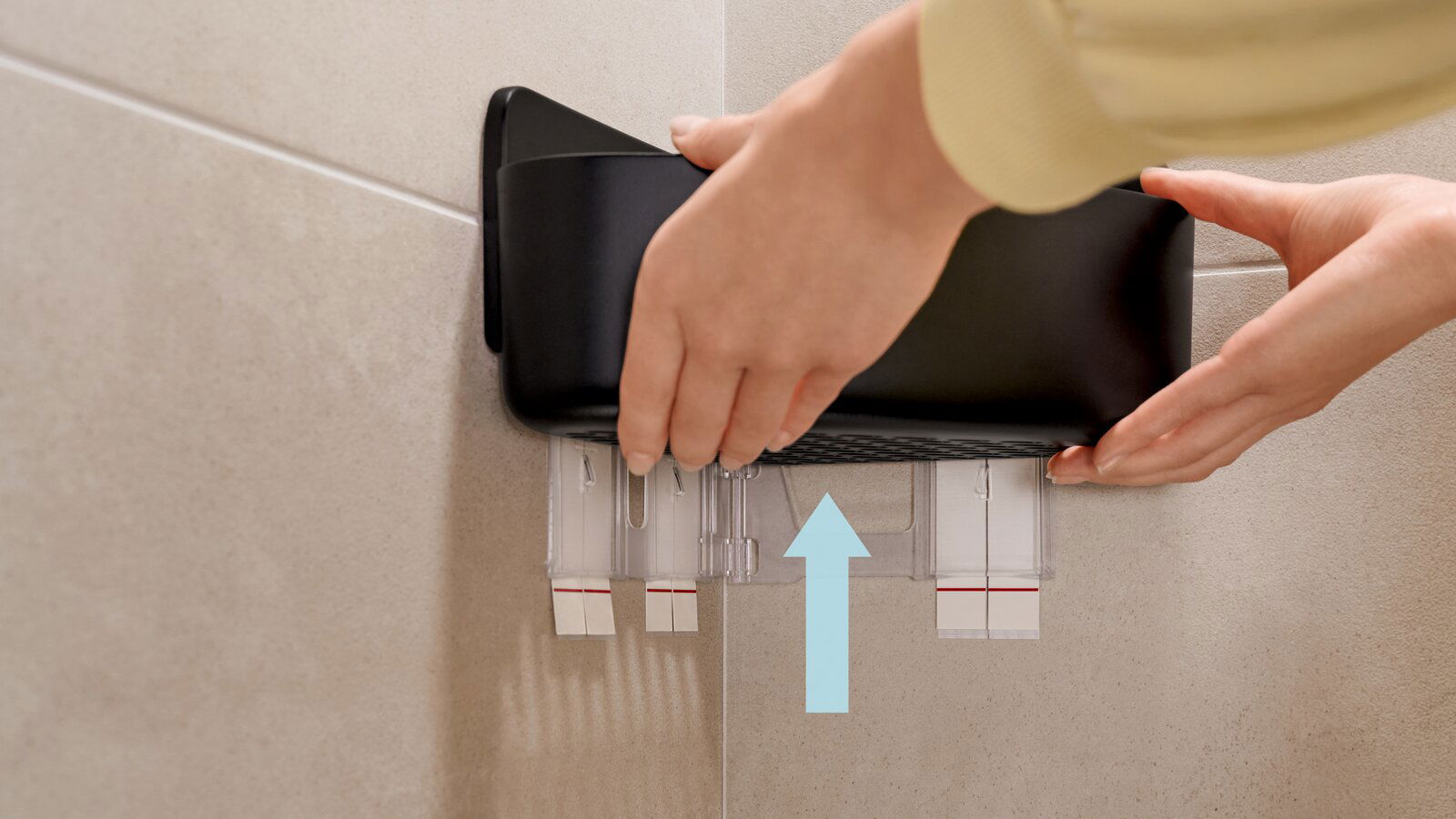 Nahaufnahme eines schwarzen Eckduschkorbs von tesa, der an einer Fliesenwand montiert wird. Hände justieren den Korb von der Seite.