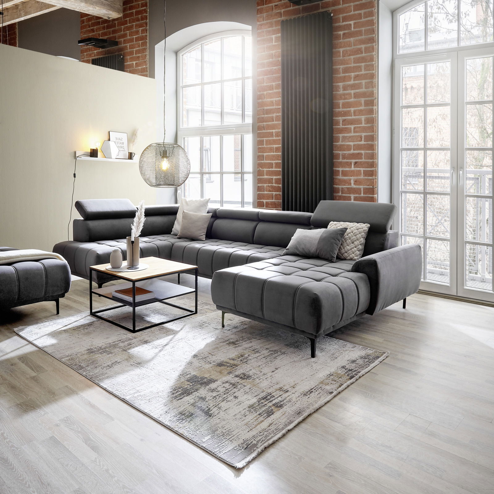 Moderne Polsterrundecke in einem stilvollen Wohnzimmer mit Backsteinwänden und großen Fenstern, seitliche Perspektive