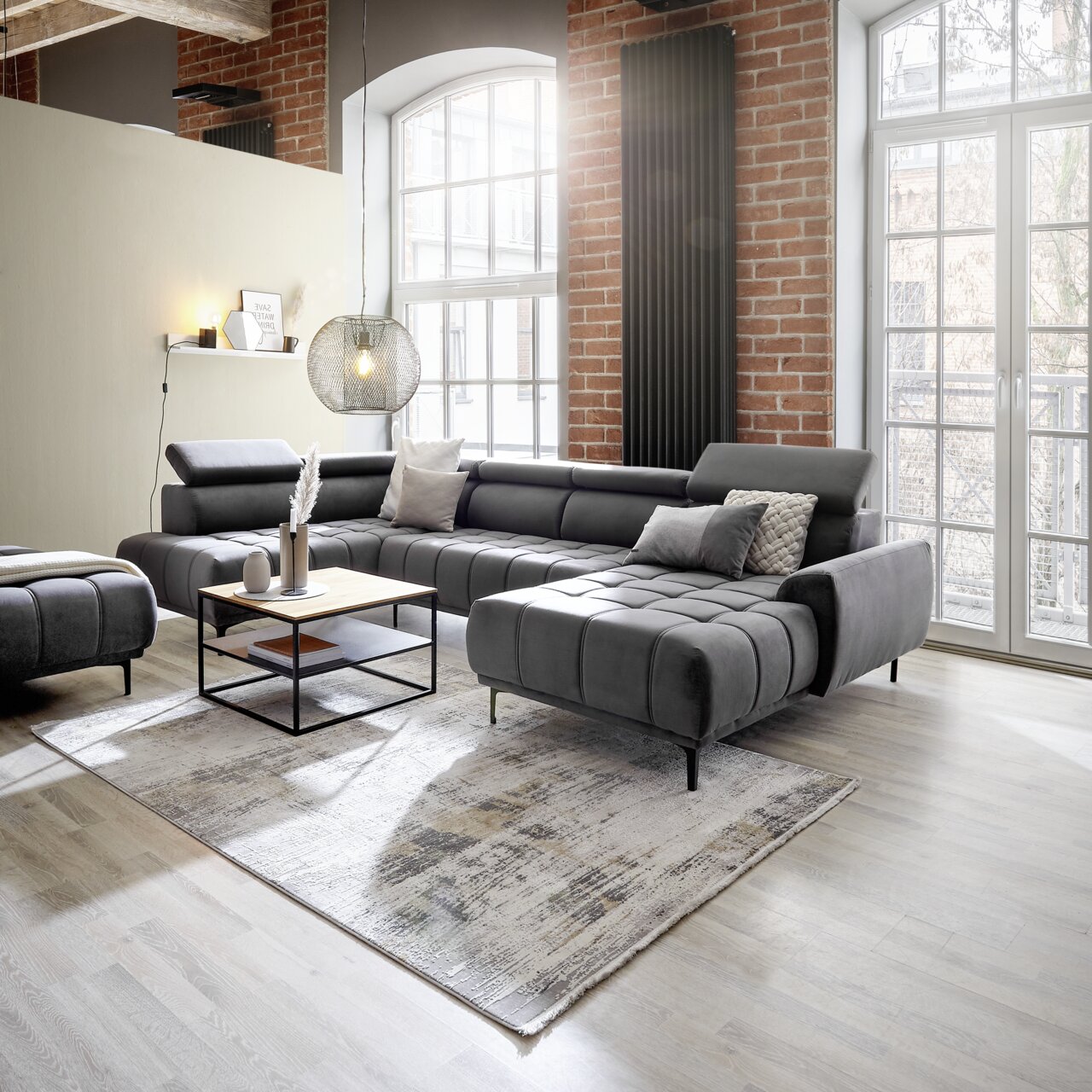 Moderne Polsterrundecke in einem stilvollen Wohnzimmer mit Backsteinwänden und großen Fenstern, seitliche Perspektive