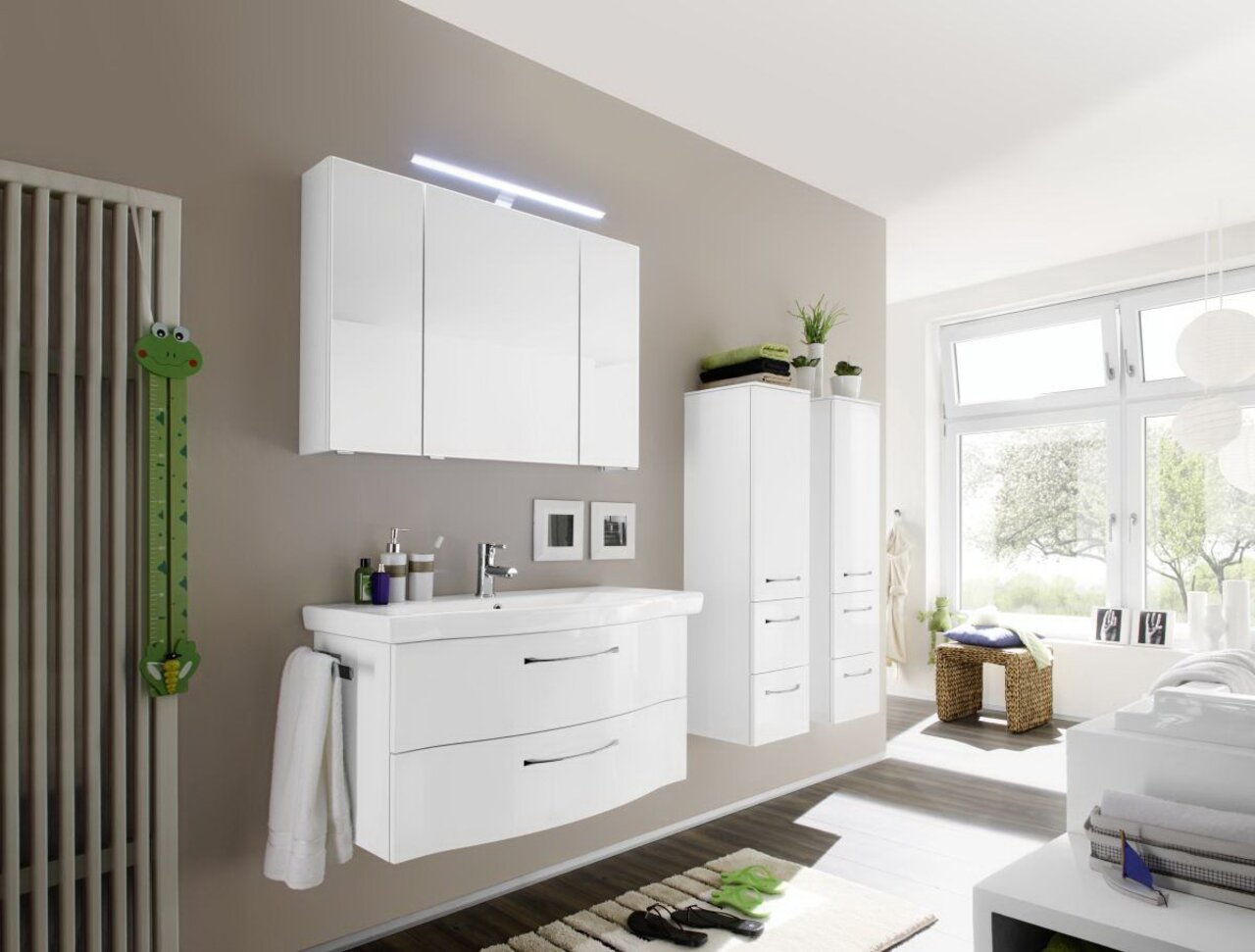 Moderne Badkombination in einem hellen Badezimmer mit Wandspiegel, Waschbeckenunterschrank und Hochschränken, seitliche Perspektive.