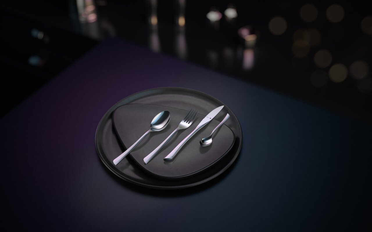 Elegantes Besteckset Virginia, bestehend aus Messer, Gabel, Löffel und Teelöffel, auf einem modernen schwarzen Teller arrangiert. Ansicht von oben.