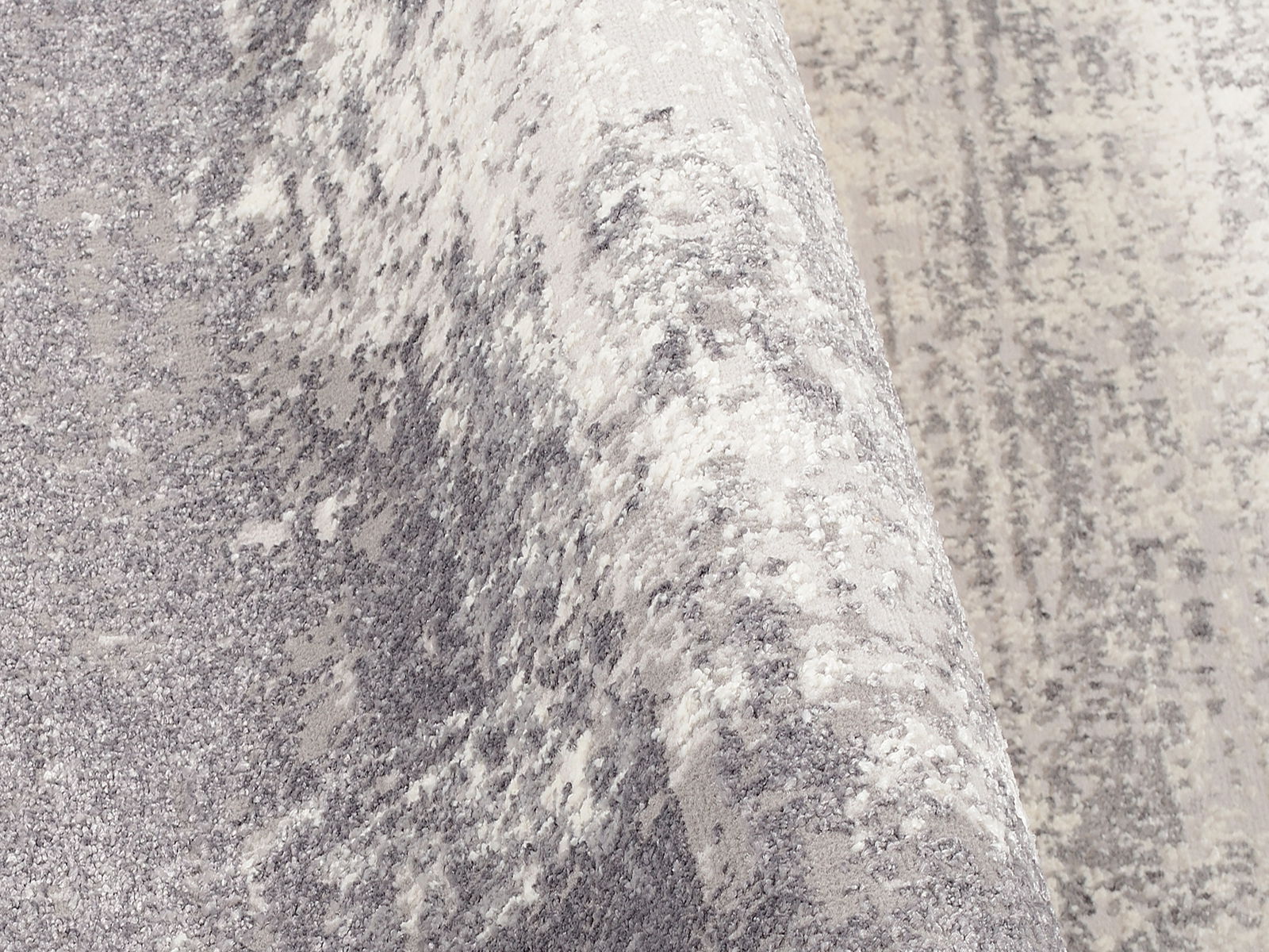 Nahaufnahme eines Designer Teppichs mit grauem und weißem Muster, perspektivisch von der Seite aufgenommen.