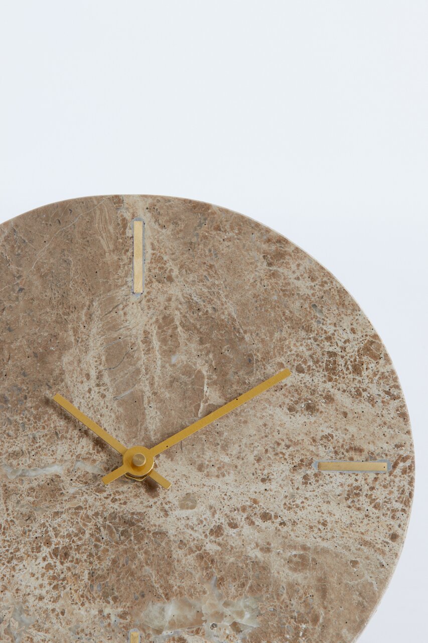 Nahaufnahme einer runden Wanduhr aus braunem Marmor mit goldenen Zeigern und minimalistischen Markierungen.