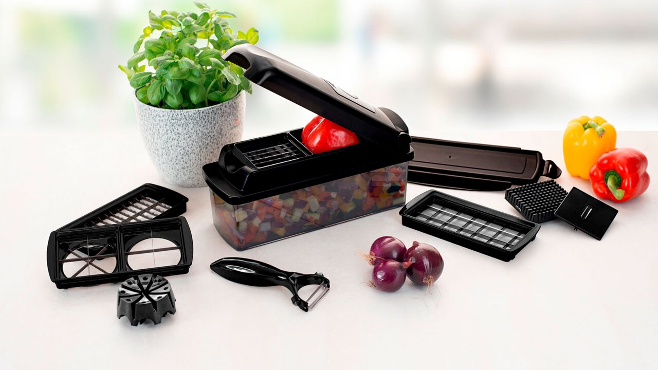 Nicer Dicer Plus Jubi 11-delige set, gezien vanuit vogelperspectief, met verschillende snij-inzetstukken, een dunschiller en gesneden groenten in een bakje.
