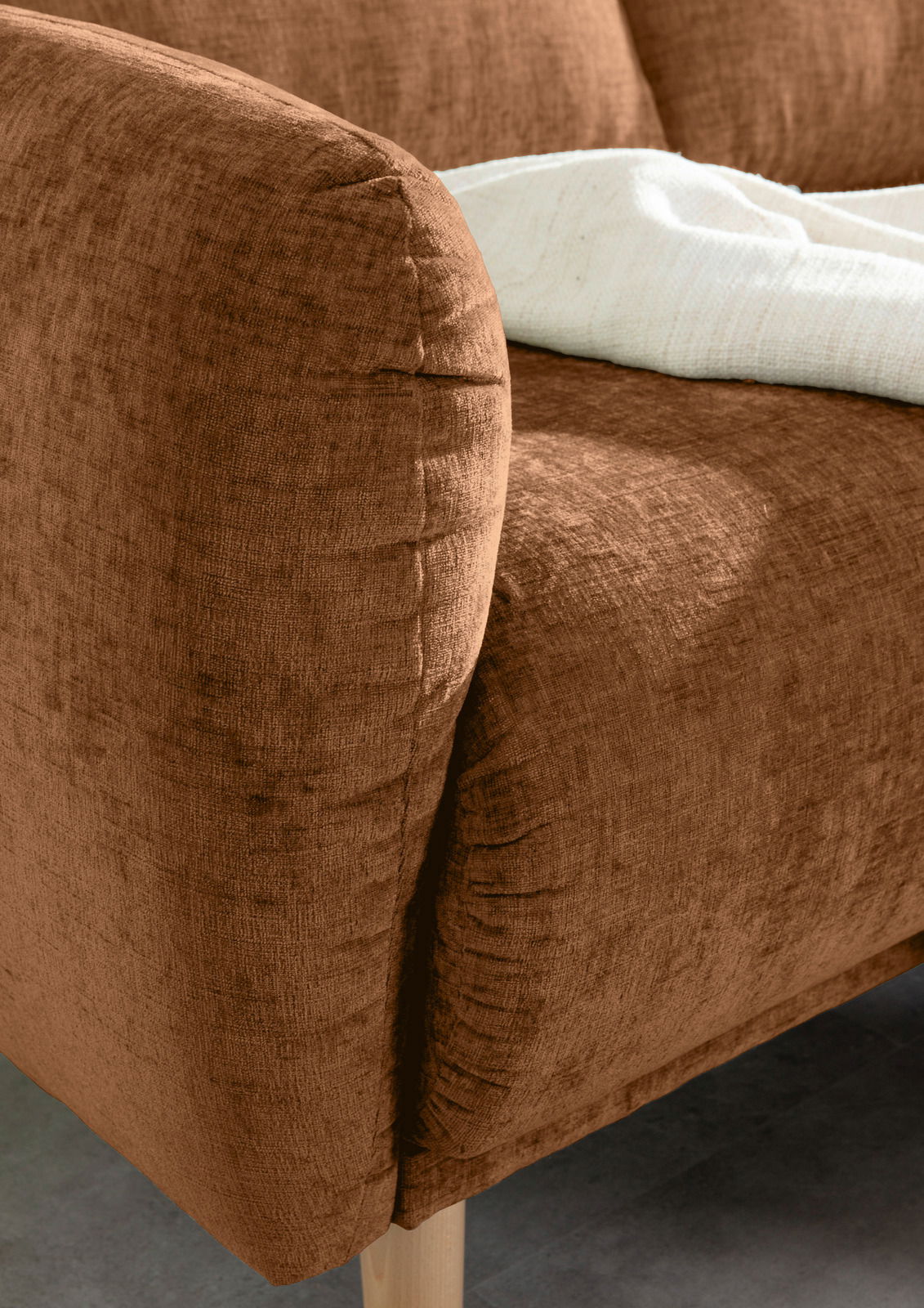 Nahaufnahme einer braunen Sofaecke mit weicher Textur und Holzbeinen, von der Seite betrachtet.
