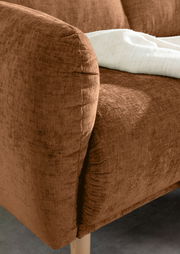 Nahaufnahme einer braunen Sofaecke mit weicher Textur und Holzbeinen, von der Seite betrachtet.