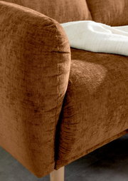 Nahaufnahme einer braunen Sofaecke mit weicher Textur und Holzbeinen, von der Seite betrachtet.