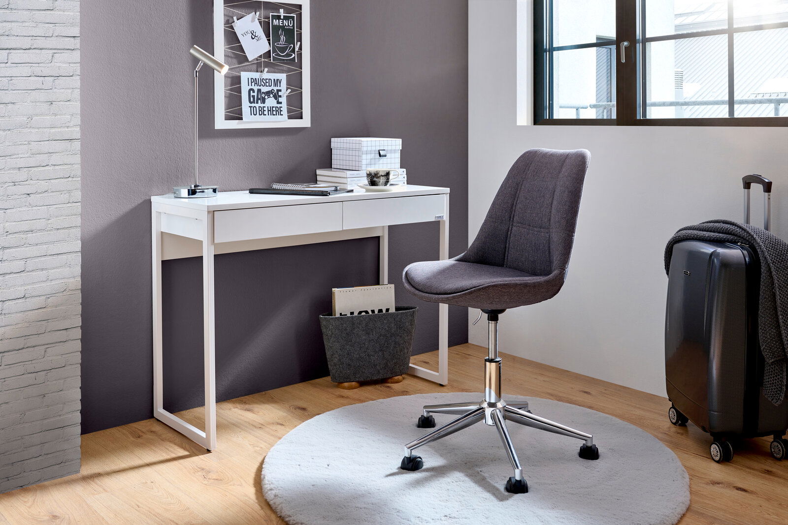 Moderner Schreibtisch in Weiß mit schlankem Design, seitliche Perspektive, ergänzt durch einen grauen Bürostuhl auf einem runden Teppich.