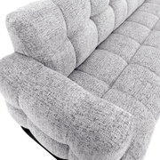 Close-up vanuit schuin bovenaanzicht van een lichtgrijze fauteuil met gemêleerde bekleding en royale, gecapitonneerde kussens