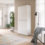Weißer, hoher Schrank mit vier grifflosen Türen in moderner Wohnzimmerecke, perspektivisch in leichter Seitenansicht von vorn fotografiert