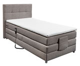 Boxspringbett in seitlicher Perspektive mit grauem Stoffbezug und weißem Topper, inklusive Fernbedienung.