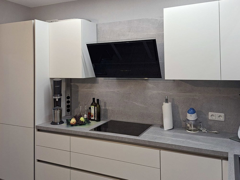 Moderne keuken met witte kasten, grijs werkblad, zwarte afzuigkap en kookplaat.