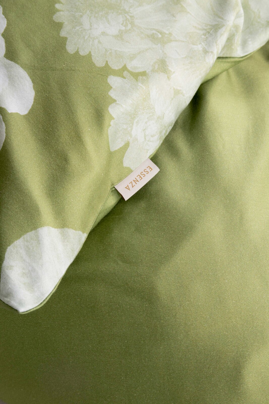 Detailaufnahme eines grünen Bettbezugs mit weißem Blumenmuster und sichtbarem ESSENZA-Label, fotografiert aus schräger Draufsicht