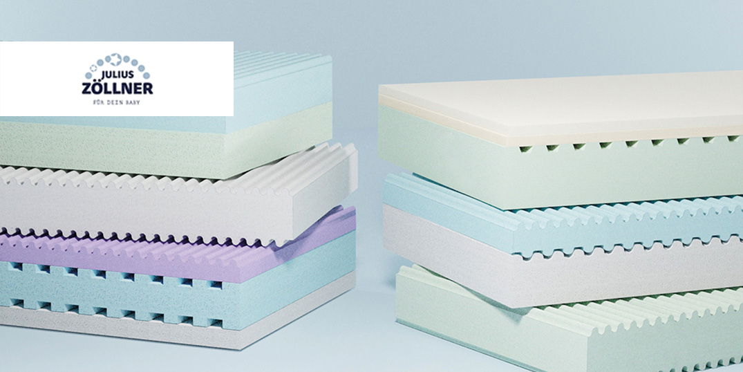 Mehrere bunte Babymatratzen mit verschiedenen Schaumstoffschichten liegen gestapelt vor blauem Hintergrund.