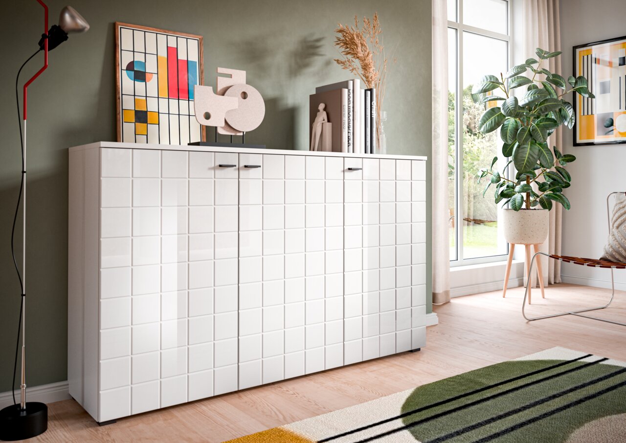 MID.YOU Sideboard MONTE Modernes weißes Sideboard mit quadratischem Muster, dekoriert mit Kunstwerken und Büchern, in einem stilvoll eingerichteten Raum mit Pflanzen und großen Fenstern, seitliche Perspektive.