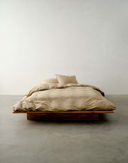 Bett mit beiger Bettwäsche in minimalistischer Umgebung, frontale Perspektive