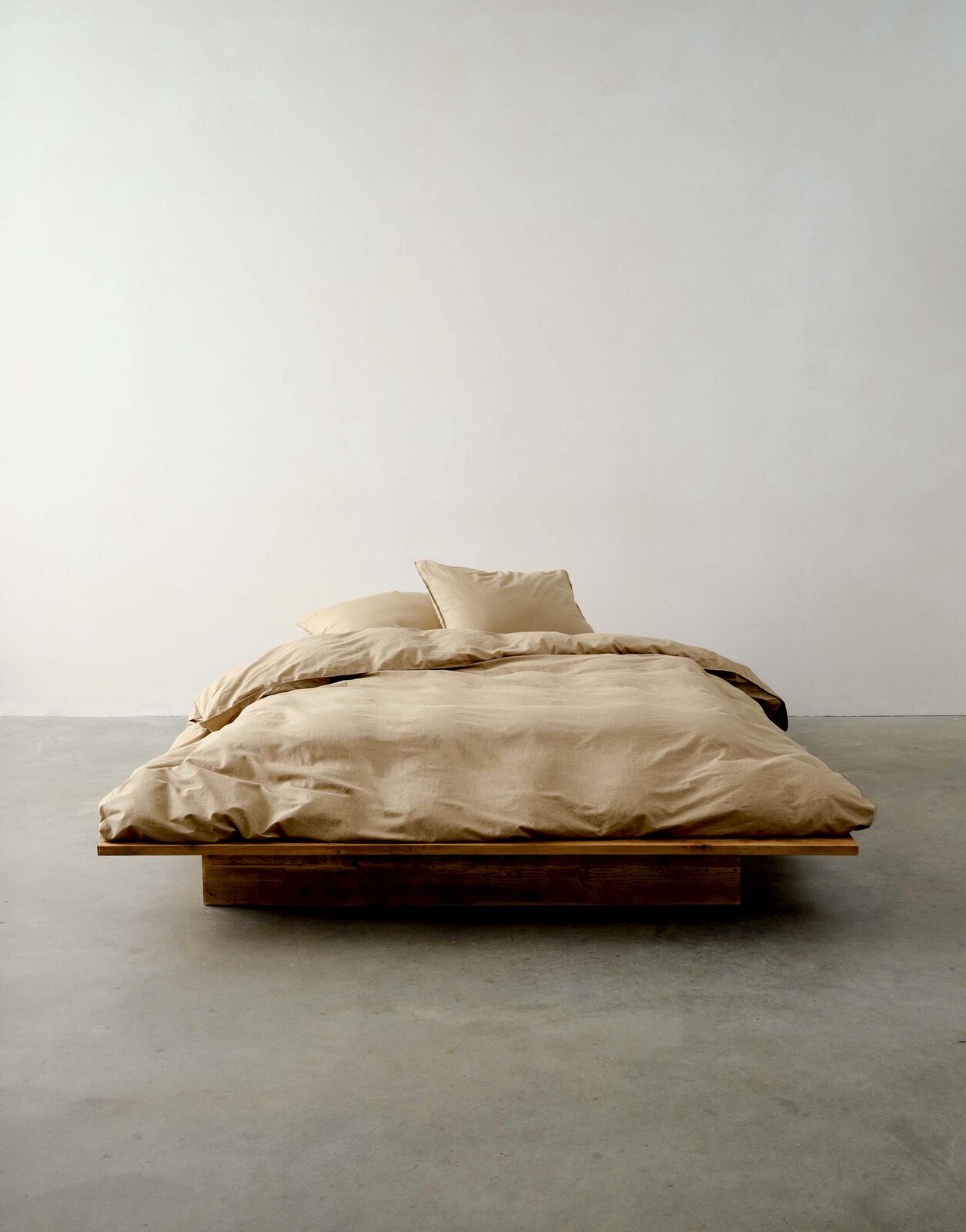 Bett mit beiger Bettwäsche in minimalistischer Umgebung, frontale Perspektive