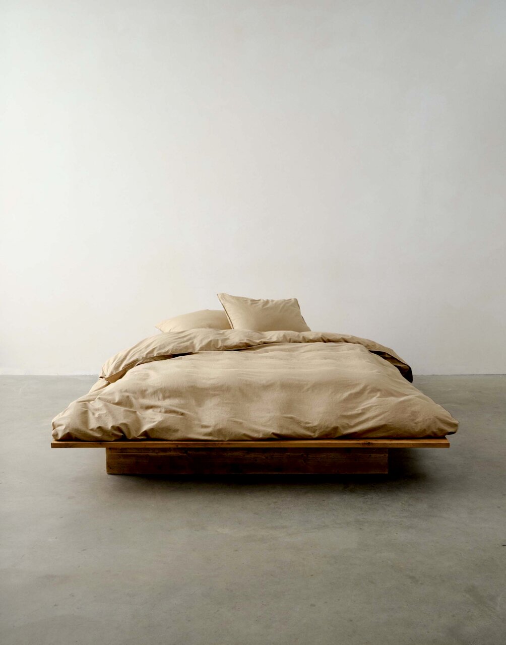 Bett mit beiger Bettwäsche in minimalistischer Umgebung, frontale Perspektive