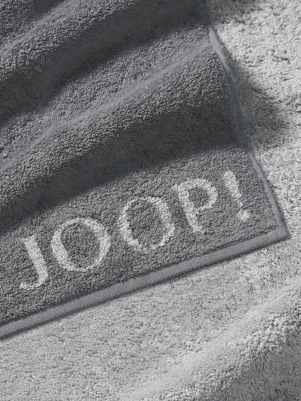 Graues Handtuch von JOOP! mit eingewebtem Logo, Nahaufnahme der Textur und Kanten.