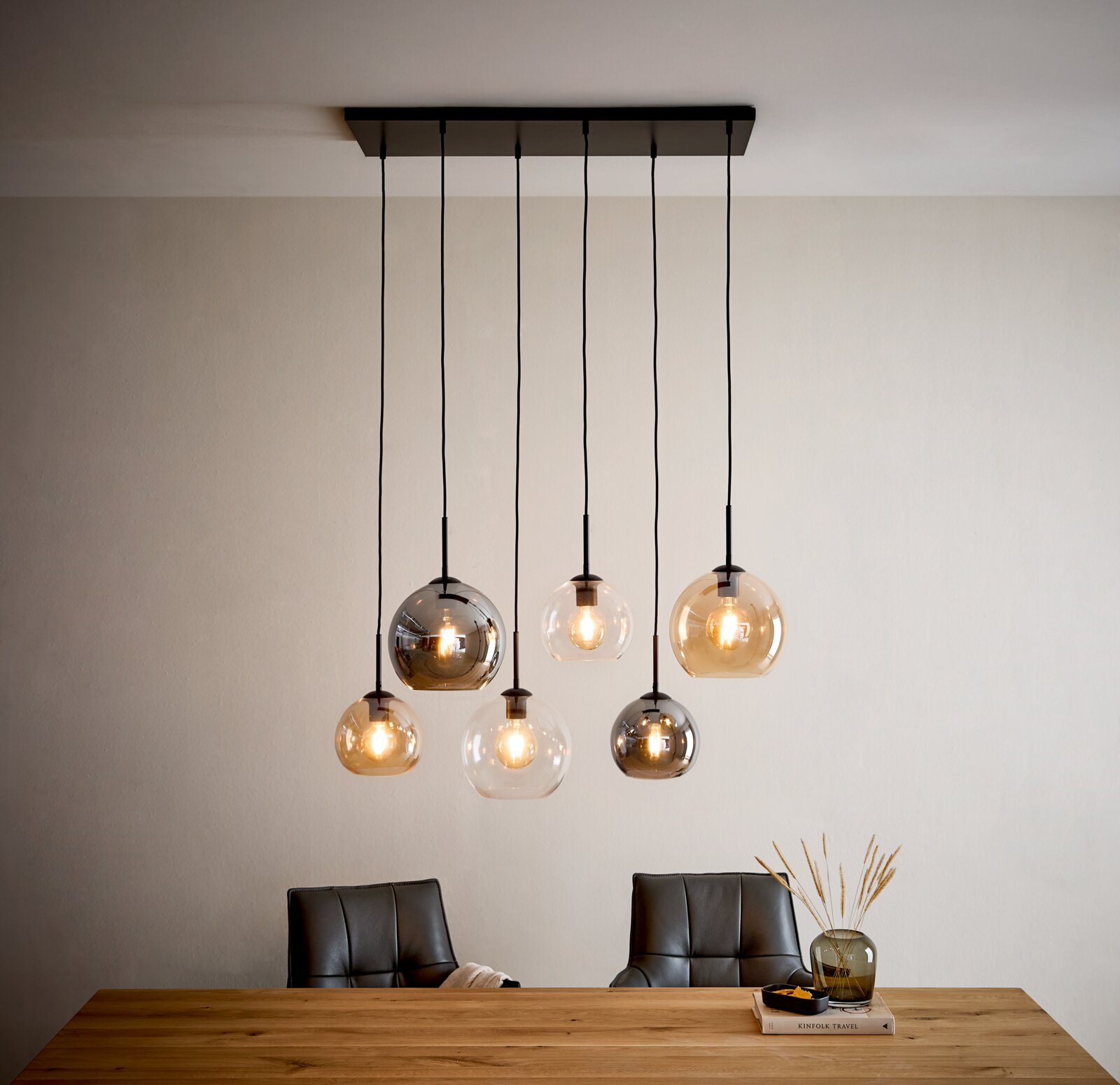 Moderne 6-flammige Pendelleuchte mit schwarzen Kabeln und Glas-Kugelschirmen in Rauchgrau, Klar und Amber über einem Esstisch, Frontansicht leicht von unten