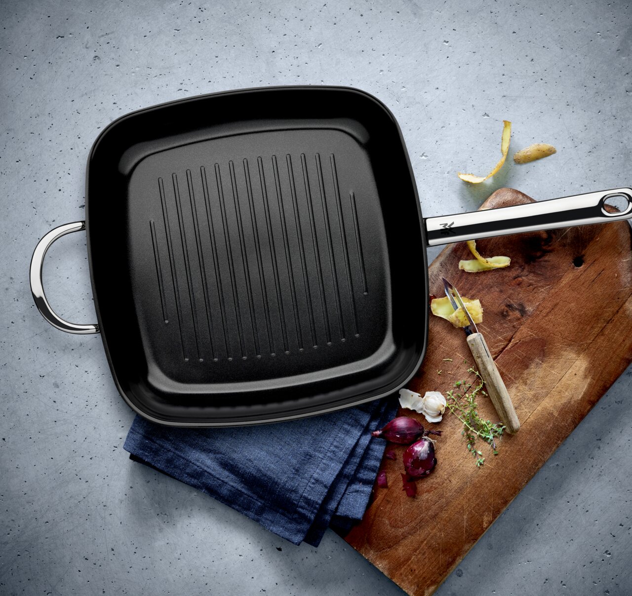 Grillpan met keramische coating, vierkant, 28 cm, gezien vanuit vogelperspectief op een theedoek en snijplank met groenten.