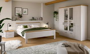 Helles Schlafzimmer-Set im Landhausstil mit Doppelbett, Nachttisch und Kleiderschrank in Weiß mit Holz-Akzenten, frontal aus leicht schräger Perspektive aufgenommen.