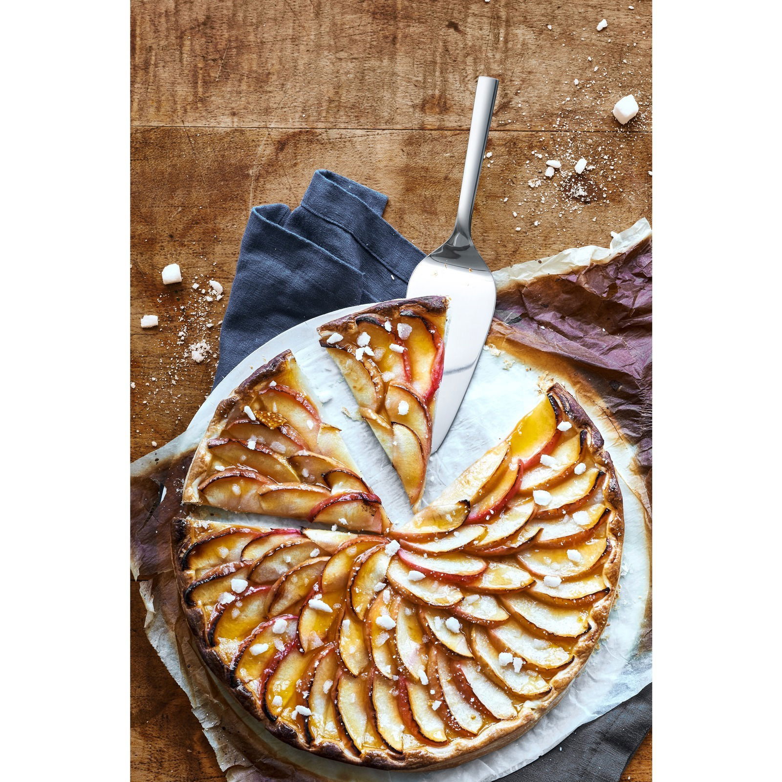 Kuchenheber aus Edelstahl, von oben fotografiert, neben einem Apfelkuchen auf einem Holztisch.