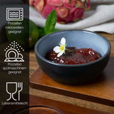 Blaue Porzellanschale mit rotem Dip und Blüte, seitliche Perspektive, umgeben von exotischen Früchten, mikrowellen- und spülmaschinengeeignet, lebensmittelecht.