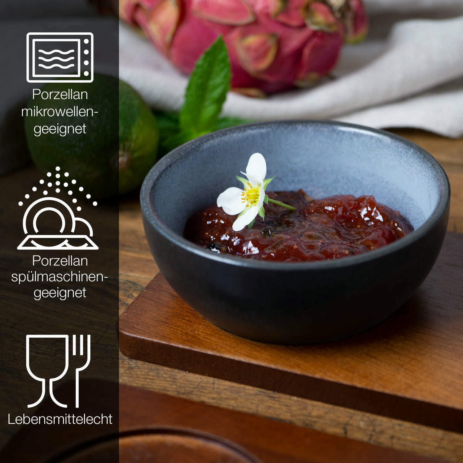 Blaue Porzellanschale mit rotem Dip und Blüte, seitliche Perspektive, umgeben von exotischen Früchten, mikrowellen- und spülmaschinengeeignet, lebensmittelecht.