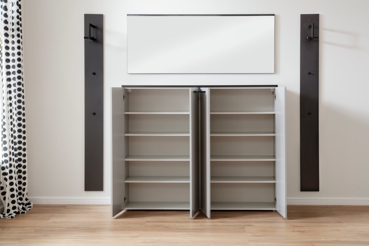 Offene Garderobe mit zwei Schränken und mehreren Regalböden, frontal fotografiert. An der Wand darüber befindet sich ein rechteckiger Spiegel, flankiert von zwei dunklen Wandpaneelen mit Haken.