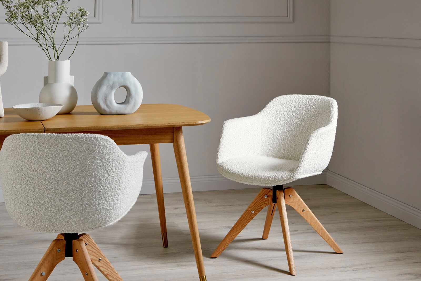 Zwei weiße Stühle mit Holzbeinen in einem modernen Esszimmer, einer von vorne und einer von hinten gesehen.