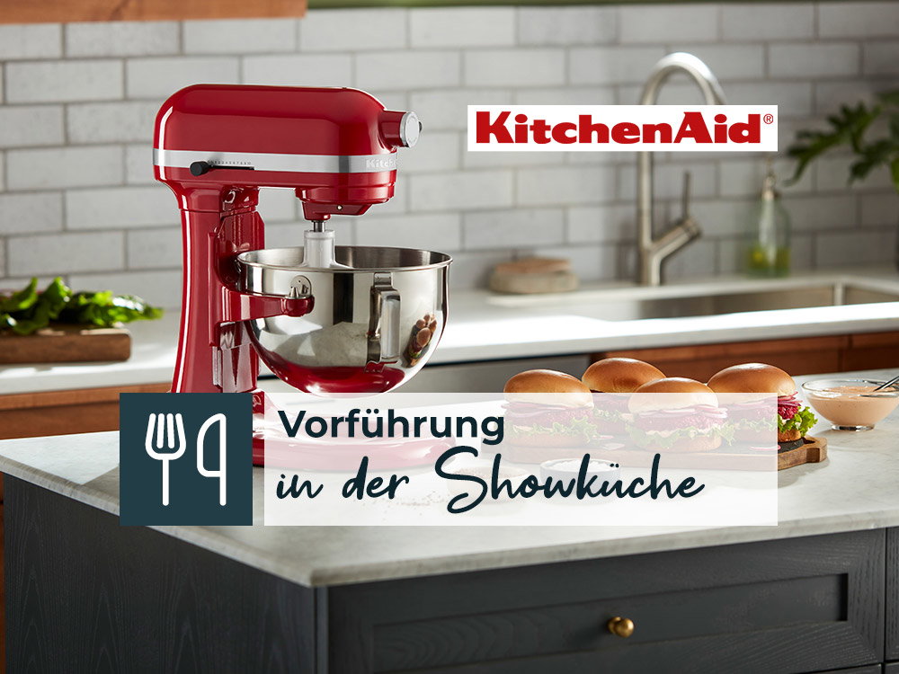 Roter Standmixer von KitchenAid auf einer Arbeitsplatte, mit Werbetext für eine Vorführung in der Showküche.