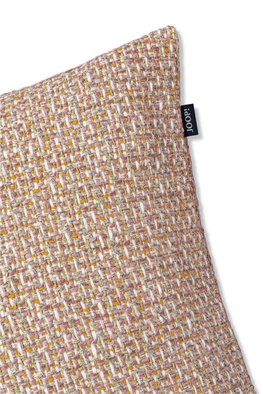 Nahaufnahme einer strukturierten Zierkissenhülle in beige und rosa Tönen mit einem kleinen schwarzen Etikett an der Seite, perspektivisch von oben rechts fotografiert.