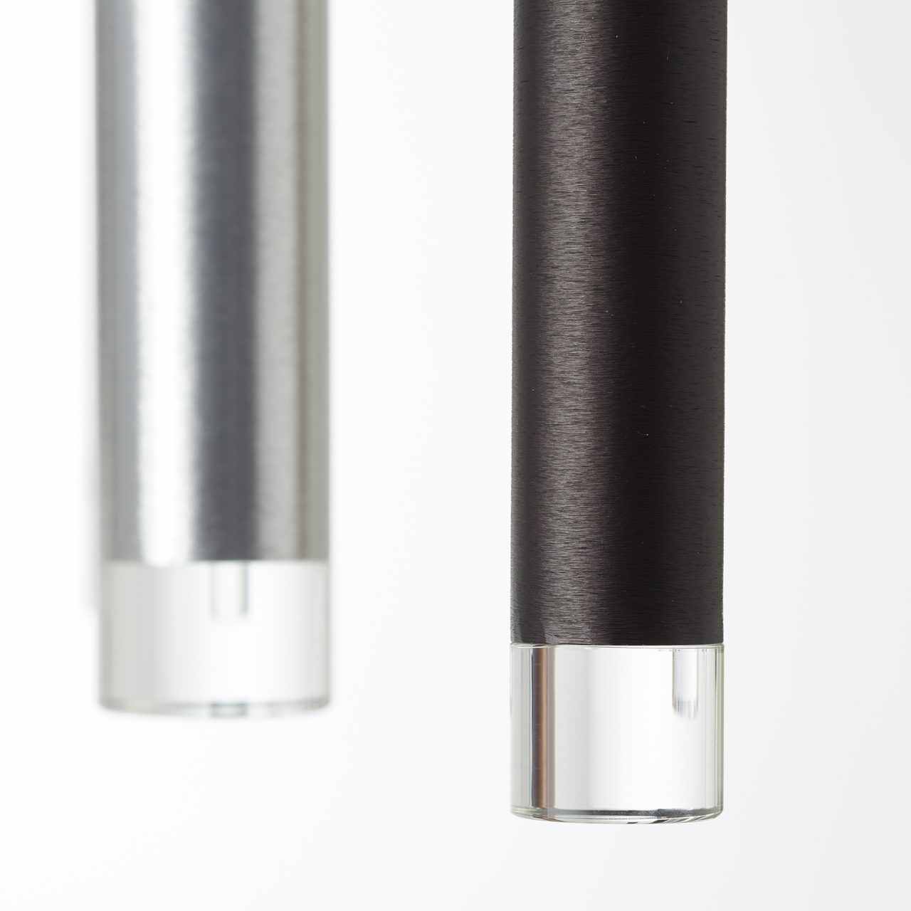 Nahaufnahme von zwei zylindrischen LED-Leuchten in Schwarz und Silber mit klaren Endkappen, seitliche Perspektive.