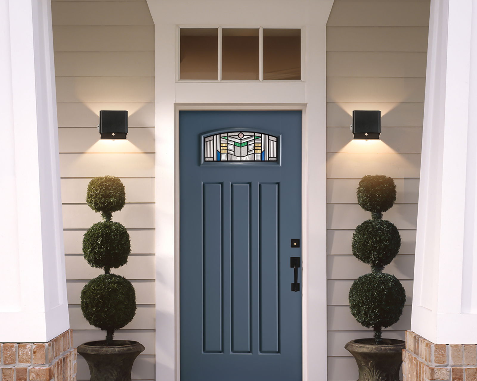 Moderne schwarze Akku-Wandleuchte an einer Hausfassade neben einer blauen Eingangstür, von vorne betrachtet.