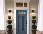 Moderne schwarze Akku-Wandleuchte an einer Hausfassade neben einer blauen Eingangstür, von vorne betrachtet.