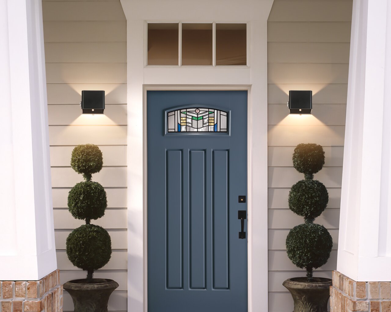 Moderne schwarze Akku-Wandleuchte an einer Hausfassade neben einer blauen Eingangstür, von vorne betrachtet.