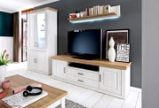 Woonkamermeubelset in landhuisstijl met een witte vitrinekast en een tv-lowboard met eikenhoutlook, een aan de muur bevestigde plank met ledverlichting en een televisie; perspectief: vooraanzicht met een lichte zijaanzicht.