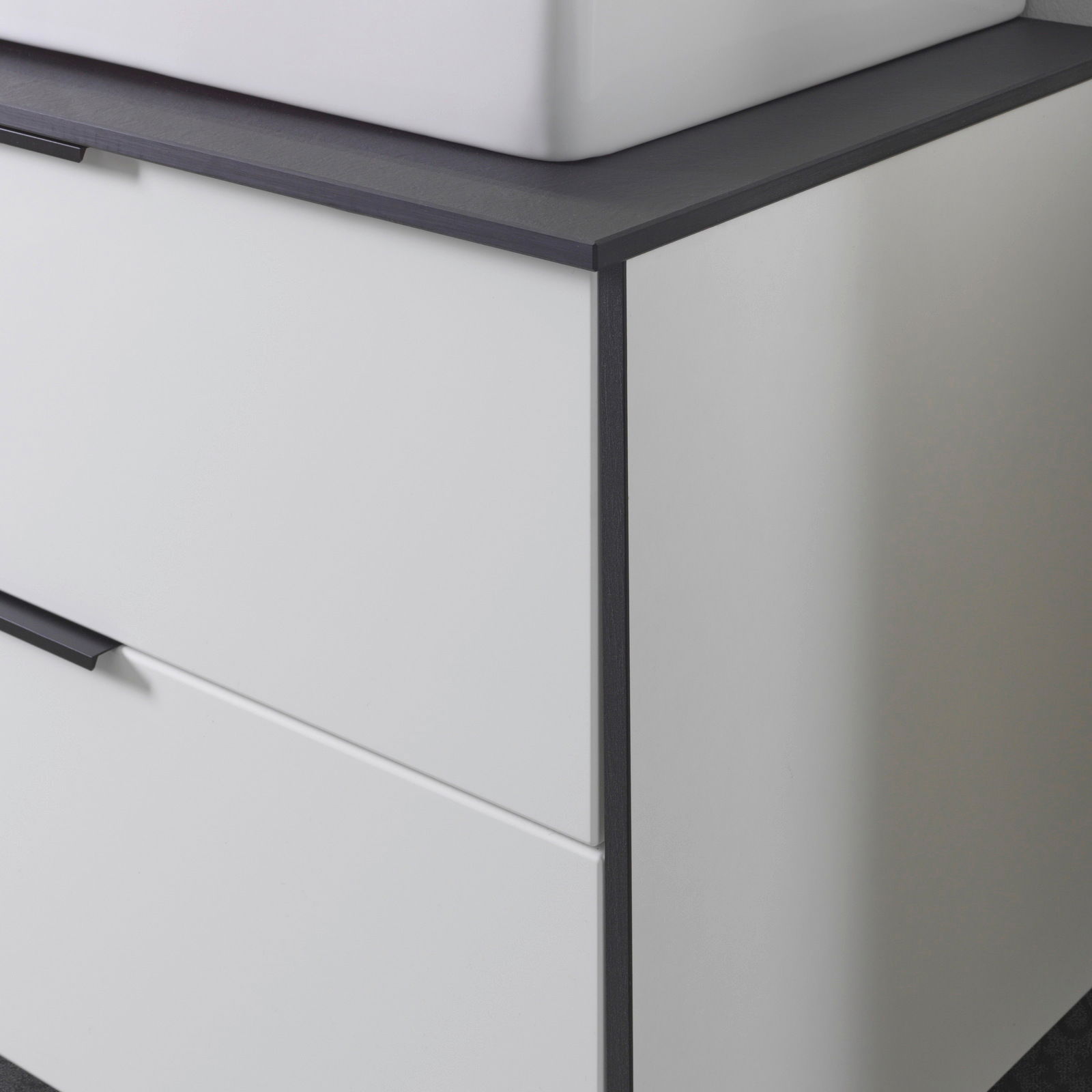 Nahaufnahme eines modernen Waschtisch-Sets mit weißem Korpus und dunkler Arbeitsplatte, seitliche Perspektive