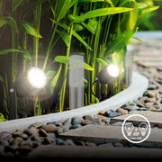 Bodenspikes Extensionset 3er S in einem Garten installiert, mit leuchtenden Strahlern entlang eines gepflasterten Weges, umgeben von grünen Pflanzen, seitliche Perspektive.