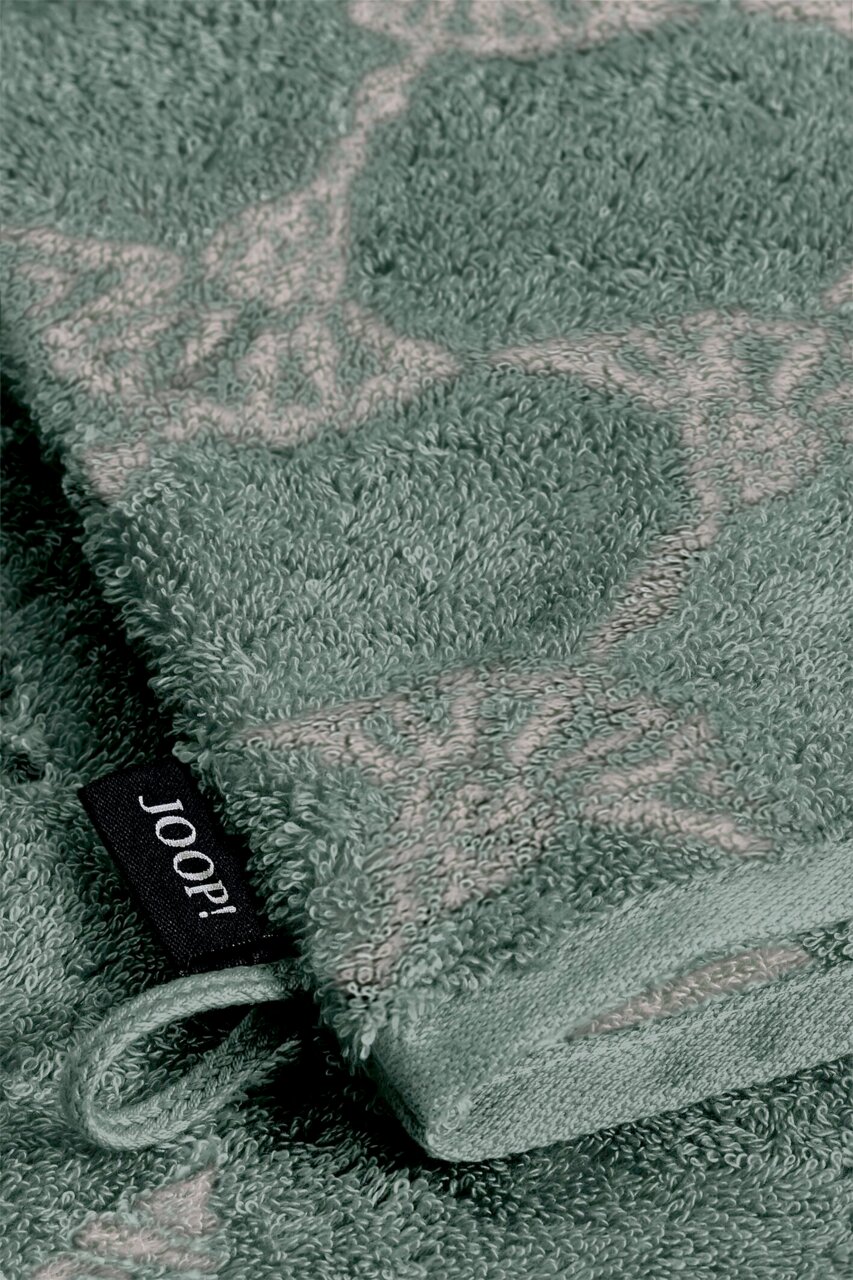 Nahaufnahme eines grünen Waschhandschuhs mit dekorativem Muster und einer schwarzen Schlaufe mit der Aufschrift 'JOOP!'.