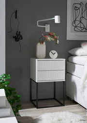 Moderne Nachtkommode mit zwei Schubladen, weiß mit geriffelter Front, auf schwarzem Metallgestell, seitliche Perspektive