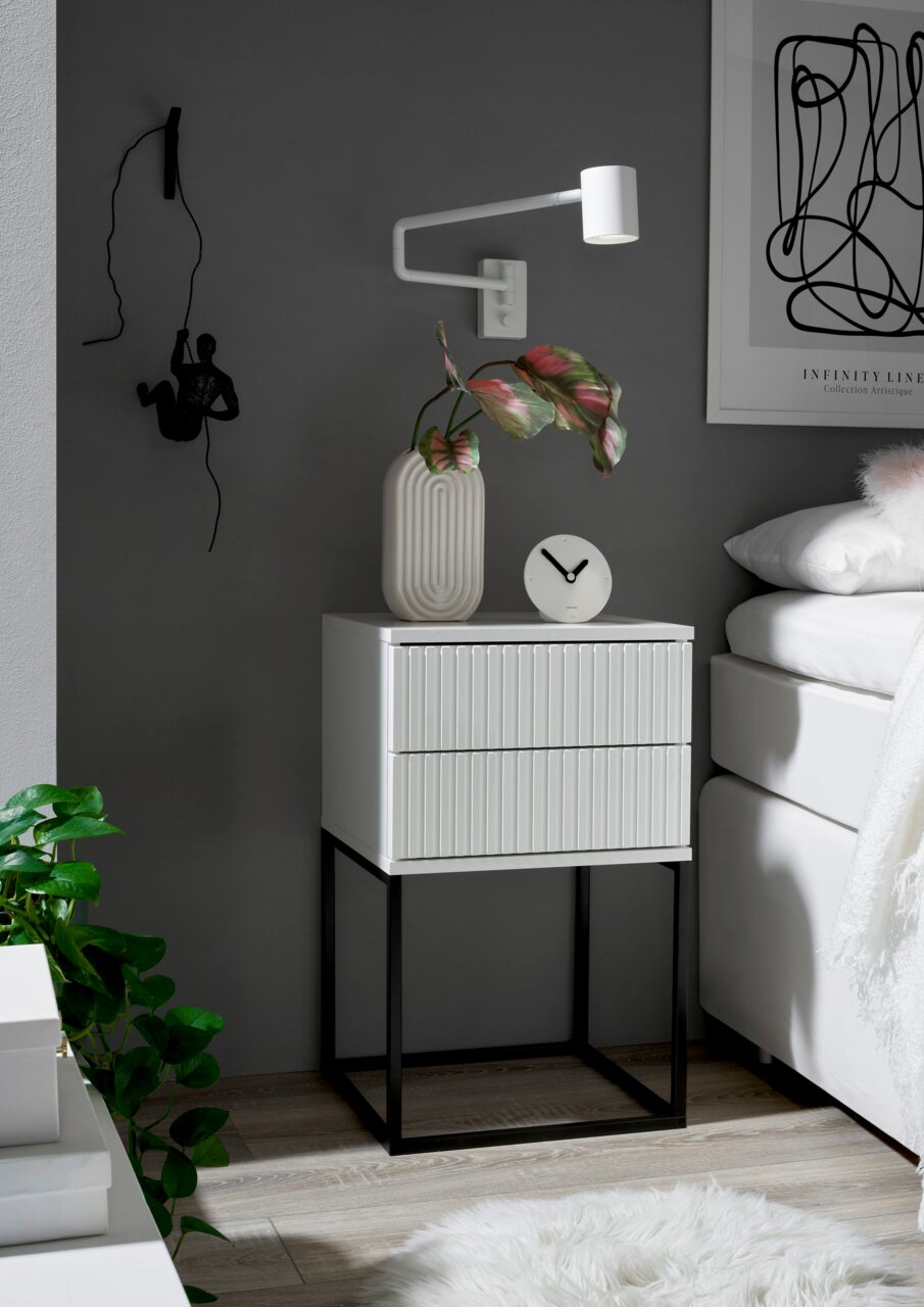 Moderne Nachtkommode mit zwei Schubladen, weiß mit geriffelter Front, auf schwarzem Metallgestell, seitliche Perspektive