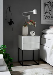 Moderne Nachtkommode mit zwei Schubladen, weiß mit geriffelter Front, auf schwarzem Metallgestell, seitliche Perspektive