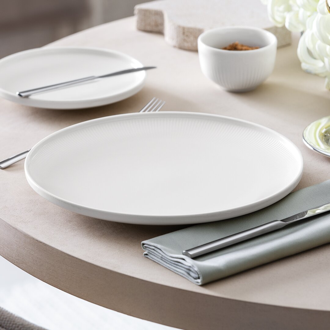 Het elegante Afina-dinerbord van 27,2 cm, gezien vanaf de zijkant op een gedekte tafel met bestek en servet.