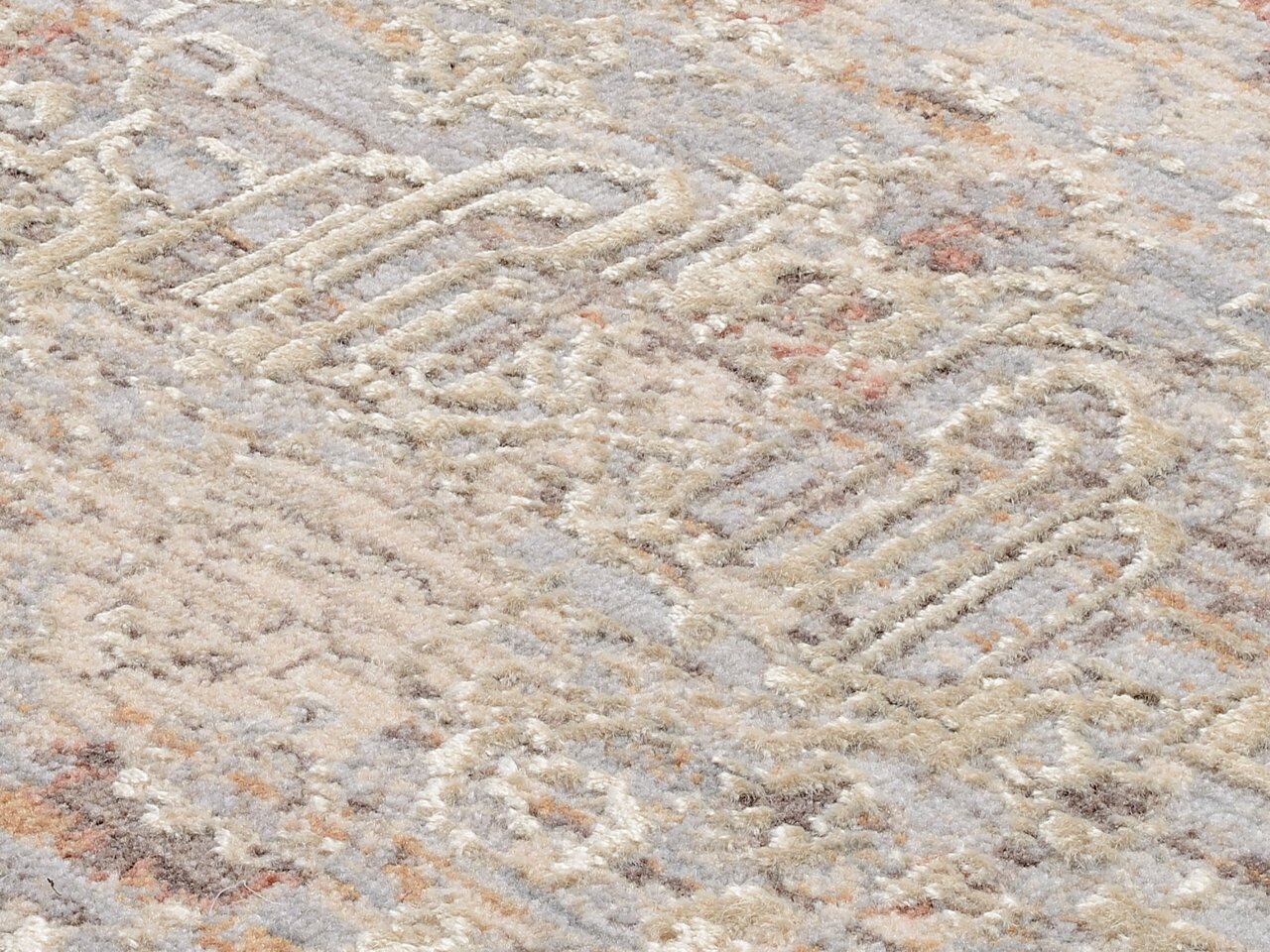 Nahaufnahme eines Designer Teppichs mit abstraktem Muster in Beige- und Grautönen, schräg von oben fotografiert.