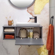 Modernes Waschtisch-Set mit grauem Schrank, weißem Waschbecken und schwarzem Wasserhahn, frontal fotografiert. Dekoriert mit Handtüchern, Zahnbürsten und Pflegeprodukten.