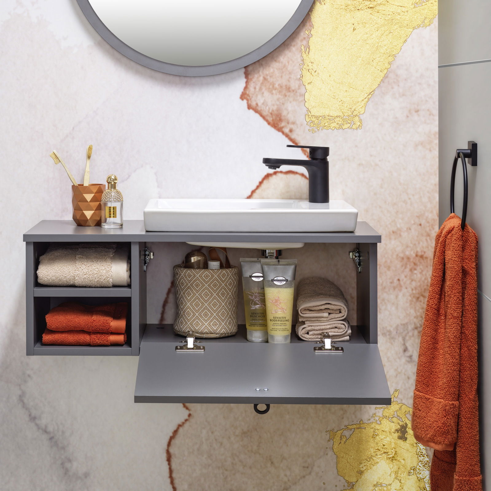 Modernes Waschtisch-Set mit grauem Schrank, weißem Waschbecken und schwarzem Wasserhahn, frontal fotografiert. Dekoriert mit Handtüchern, Zahnbürsten und Pflegeprodukten.