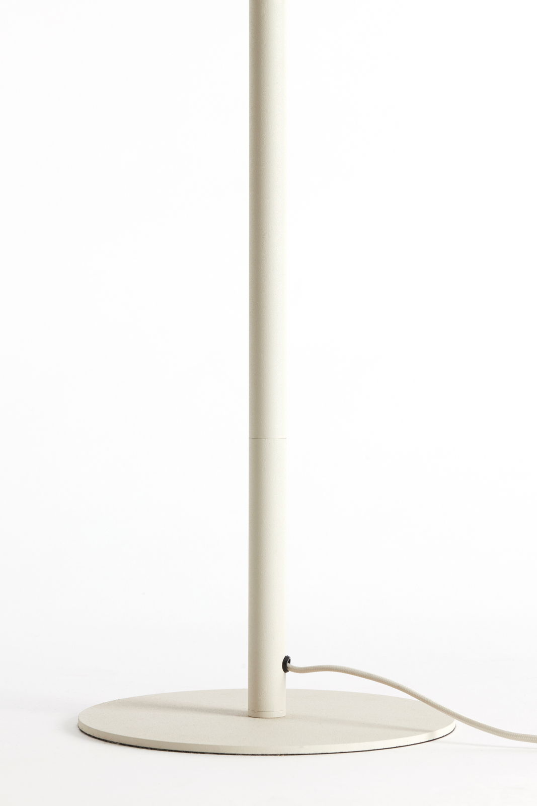 Nahaufnahme des unteren Teils einer Stehleuchte mit rundem Sockel und Stromkabel, seitliche Perspektive.